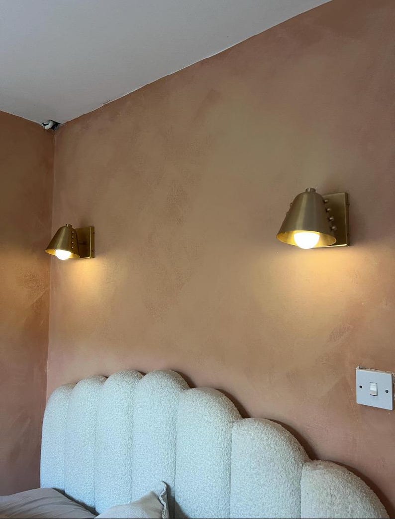 A Decorative Wine Colored Cone Wall Lamp with Handcrafted Brass Construction, Photographed to Highlight Its Compact Proportions, Tapered Shade, and Distinctive Rivet Details in A Mid Century Inspired Form, Frost Lights.