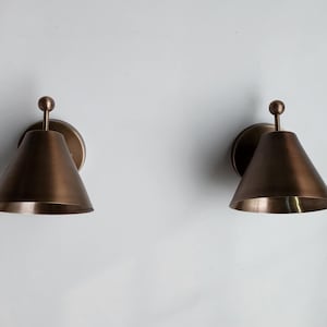 Side Angled View of The Vintage Inspired Brass Wall Sconce Pair, Showing the 9 Inch Depth and Decorative Finial Elements. Each Handmade Fixture Has a Solid Brass Body and Round Canopy, Creating a Balanced Classic Form for Indoor Residential or Commercial Spaces, Frost Lights.