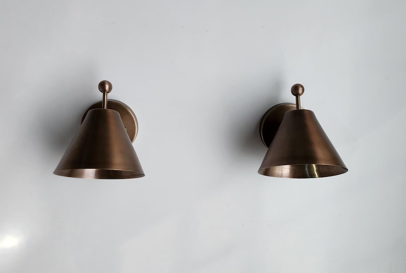 Side Angled View of The Vintage Inspired Brass Wall Sconce Pair, Showing the 9 Inch Depth and Decorative Finial Elements. Each Handmade Fixture Has a Solid Brass Body and Round Canopy, Creating a Balanced Classic Form for Indoor Residential or Commercial Spaces, Frost Lights.