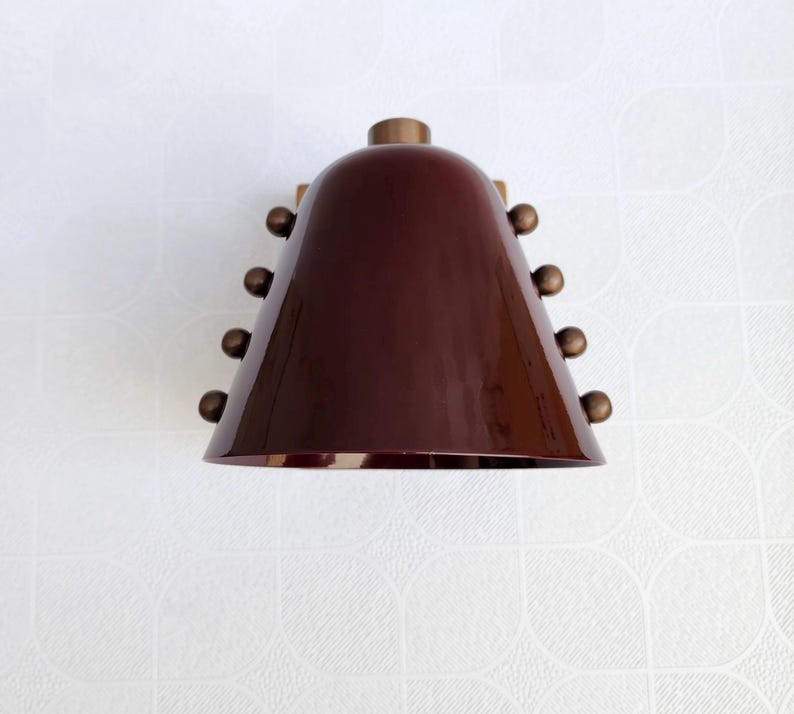 A Decorative Wine Colored Cone Wall Lamp with Handcrafted Brass Construction, Photographed to Highlight Its Compact Proportions, Tapered Shade, and Distinctive Rivet Details in A Mid Century Inspired Form, Frost Lights.