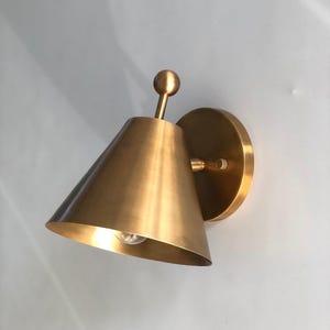 A Pair of Handmade Brass Wall Sconces Is Shown from An Angled View, Highlighting the Decorative Finial Details and Solid Brass Construction. the Classic Fixtures Have a Refined Silhouette Designed for Balanced Wall Lighting in Bedrooms, Hallways, Living Rooms, and Traditional Interiors, Frost Lights.