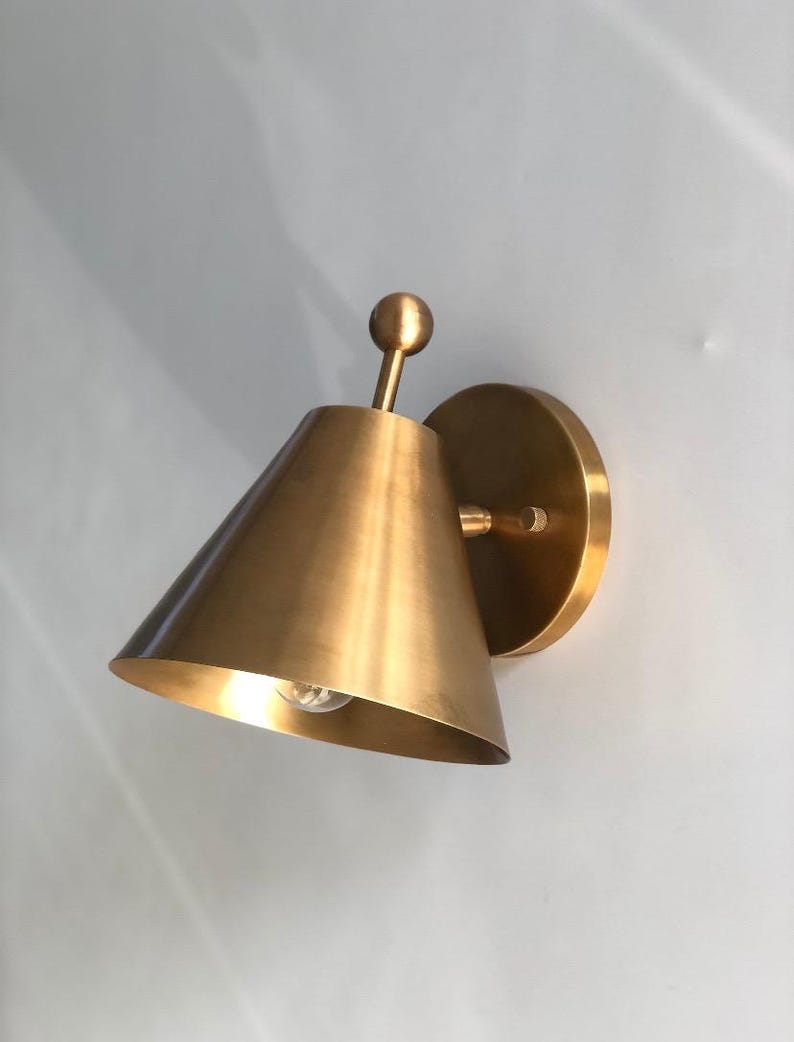 A Pair of Handmade Brass Wall Sconces Is Shown from An Angled View, Highlighting the Decorative Finial Details and Solid Brass Construction. the Classic Fixtures Have a Refined Silhouette Designed for Balanced Wall Lighting in Bedrooms, Hallways, Living Rooms, and Traditional Interiors, Frost Lights.