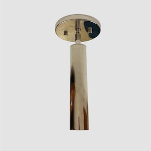 Peut inclure: Un luminaire de plafond en métal doré poli doté d'une rosace de montage circulaire et d'un boîtier de suspension cylindrique allongé. La surface est hautement réfléchissante, présentant des courbes métalliques lisses et deux petites vis.