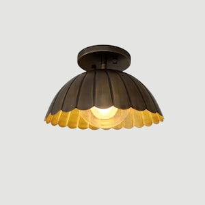 Può includere: Un lampadario da soffitto color bronzo con un paralume a forma di cupola smerlata. La lampada ha una base rotonda e un design a coste sul paralume. L'interno del paralume è dorato e all'interno è visibile una lampadina.
