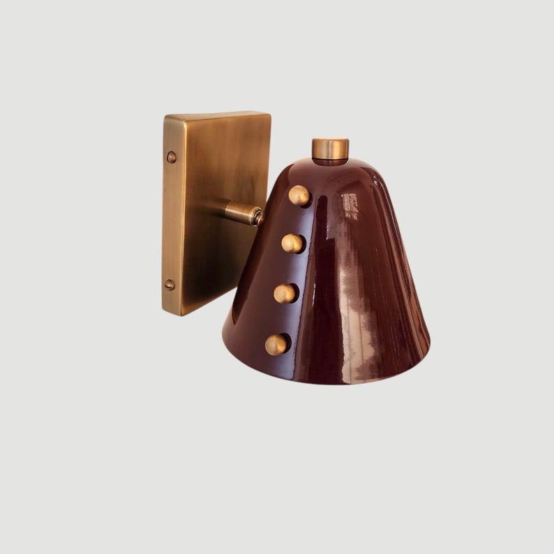 A Wine Cone Wall Sconce Featuring a Warm Brass Structure and Small Decorative Rivets Around the Tapered Shade, Photographed to Highlight Its Compact Proportions and Distinctive Mid Century Inspired Design, Frost Lights.
