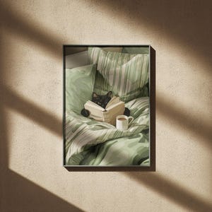 May include: A framed print featuring a black cat reading a book in bed. The cat is nestled among green and white patterned bedding, with a small white mug of coffee nearby. The overall aesthetic is cozy and inviting.