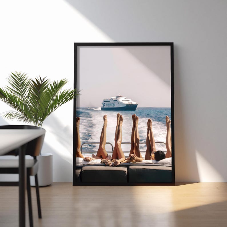 May include: Framed print featuring a group of people with their legs raised in the air on a boat, with a ferry in the background. The image has a sunny, vacation vibe, with blue water and sky.