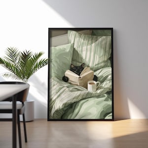 May include: A framed print depicts a black cat reading a book in bed. The cat is surrounded by green and white striped bedding and pillows. A white mug with a brown beverage sits nearby. The artwork is displayed in a room with a plant.