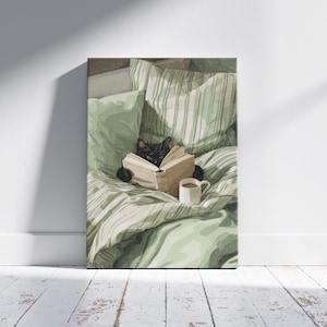 May include: A canvas print depicts a black cat reading a book in bed, surrounded by green pillows and a striped comforter. A white mug with a brown beverage sits nearby. The artwork is displayed against a white wall and a wooden floor.