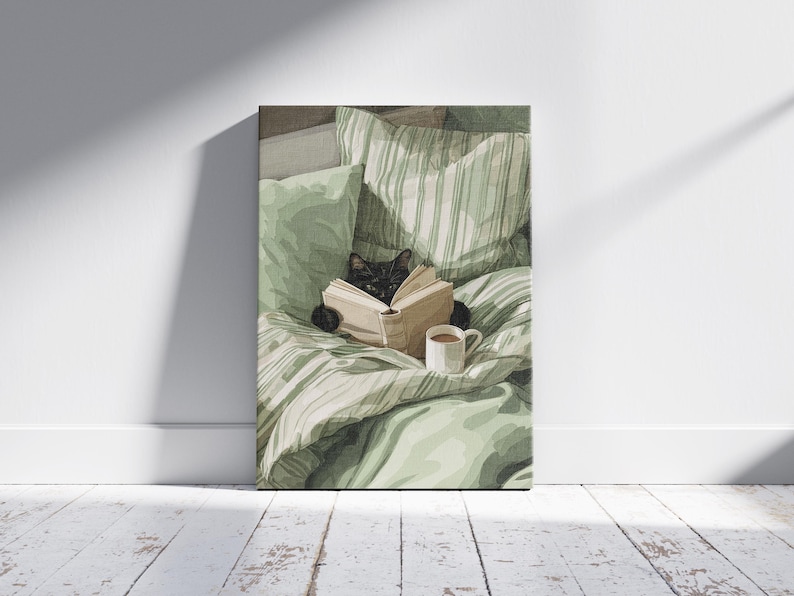 May include: A canvas print depicts a black cat reading a book in bed, surrounded by green pillows and a striped comforter. A white mug with a brown beverage sits nearby. The artwork is displayed against a white wall and a wooden floor.
