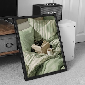 May include: Framed art print featuring a black cat reading a book in bed. The cat is nestled among green and white striped bedding, with a mug of coffee nearby. The artwork is in a black frame, with a speaker and cabinet in the background.