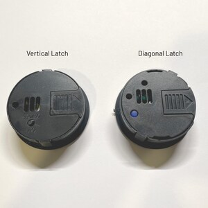 May include: Two black round plastic covers with latches. The cover on the left has a vertical latch and the cover on the right has a diagonal latch. Both covers have a small blue indicator light.