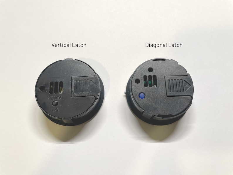 May include: Two black round plastic covers with latches. The cover on the left has a vertical latch and the cover on the right has a diagonal latch. Both covers have a small blue indicator light.