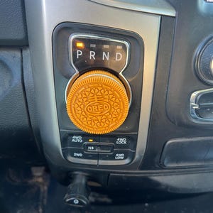 Könnte beinhalten: Nahaufnahme eines Automatik-Wählhebels mit einem Oreo-Keks auf dem Knauf. Der Wählhebel hat die Buchstaben "P", "R", "N" und "D" darauf. Die 4WD-Steuerung des Autos ist unter dem Wählhebel sichtbar.