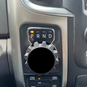 Può includere: Primo piano della console del cambio di un veicolo. La console presenta un selettore di marcia con indicatori "PRND", illuminati in giallo. Sotto ci sono pulsanti per 4WD Auto, 4WD Lock, 2WD e 4WD Low. È presente una manopola di controllo circolare nera.