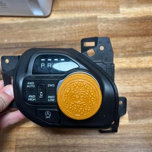 May include: A black plastic car gear shifter with a round knob. The knob is orange and has the word "OREO" printed on it. The shifter has buttons for 4WD Auto, 4WD High, 4WD Low, 2WD, and an off button.