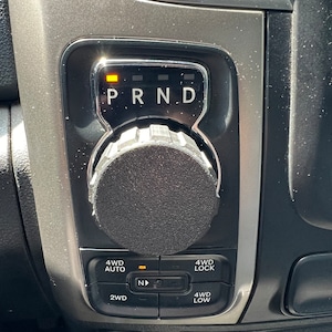 Può includere: Primo piano del cambio di marcia di un'auto con le lettere "P R N D" visualizzate. Il cambio ha una manopola con una presa in gomma nera. L'auto ha un sistema 4WD con pulsanti per 4WD Auto, 4WD Lock, 2WD e 4WD Low.