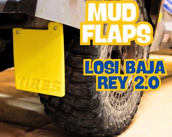 Puede incluir: Guardabarros amarillos con la palabra "TIRES" impresa en ellos, unidos a la rueda trasera de un coche RC Losi Baja Rey 2.0 negro. El texto "MUD FLAPS" y "LOSI BAJA REY 2.0" está impreso en blanco sobre fondo amarillo.