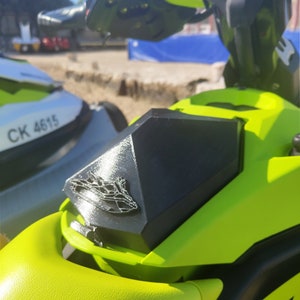 May include: Close-up of a black and green jet ski with a black, diamond-shaped cover over the gas tank. The cover has a silver logo of a jet ski on it. The jet ski has the registration number "CK 4615" on the side.