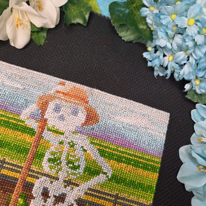 May include: A cross-stitch design featuring a skeleton wearing a straw hat and holding a wooden staff, set against a backdrop of a field and sky. The skeleton is white, the hat is brown, and the field is green and yellow.