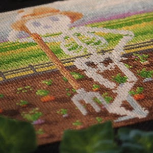 May include: Cross-stitch art depicting a skeleton farmer wearing a straw hat, holding a pitchfork, and tending a garden. The scene features a brown garden bed with green and orange plants, a wooden fence, and a colorful sky.