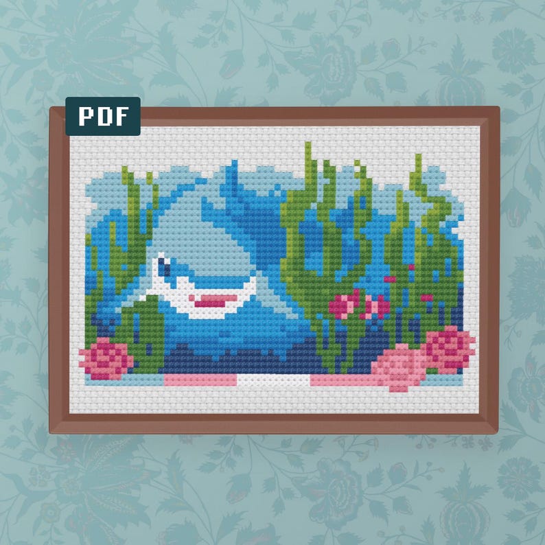 May include: Cross-stitch design of a shark underwater, in a brown frame. The image shows a blue shark, green seaweed, and pink coral. The upper left corner has the word "PDF".