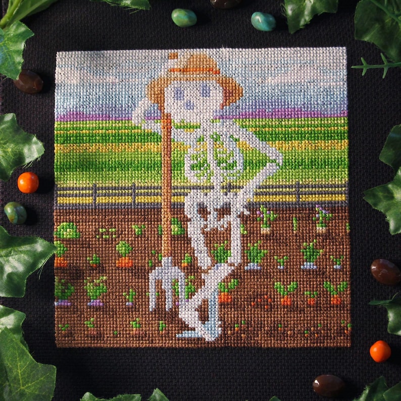 May include: Cross-stitch artwork depicting a skeleton farmer in a field. The skeleton wears a straw hat and leans on a pitchfork. The scene includes a brown field with green plants, a wooden fence, and a colorful sky. The artwork is square.