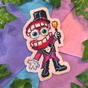 Peut inclure: Un écusson au point de croix représentant un personnage de dessin animé avec une grosse tête, un large sourire et des yeux dépareillés, l'un bleu et l'autre vert. Il porte un haut-de-forme noir et un costume magenta avec une chemise blanche.