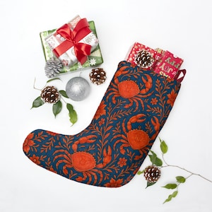 May include: A Christmas stocking with a navy blue background and a pattern of orange crabs and floral elements. The stocking is filled with wrapped gifts and pine cones. Additional gifts and ornaments are arranged around the stocking.
