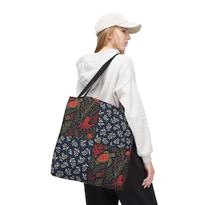 May include: A navy tote bag with a marine life pattern featuring red octopuses, turtles, and coral. The bag has a black shoulder strap and a white background.
