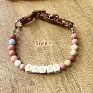 May include: A dog collar with a brown leather strap and gold-colored hardware. The collar features a strand of colorful beads and white lettered beads that spell "DAICE". The text "Style 4" is also visible.