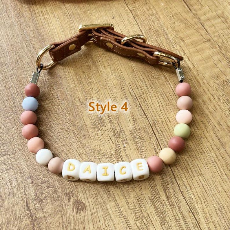May include: A dog collar with a brown leather strap and gold-colored hardware. The collar features a strand of colorful beads and white lettered beads that spell "DAICE". The text "Style 4" is also visible.