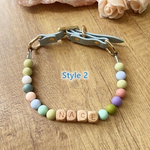 May include: A light blue dog collar with gold-colored hardware and a beaded section. The beads are pastel colors, and the wooden letter beads spell out "NACE". The text "Style 2" is also visible.