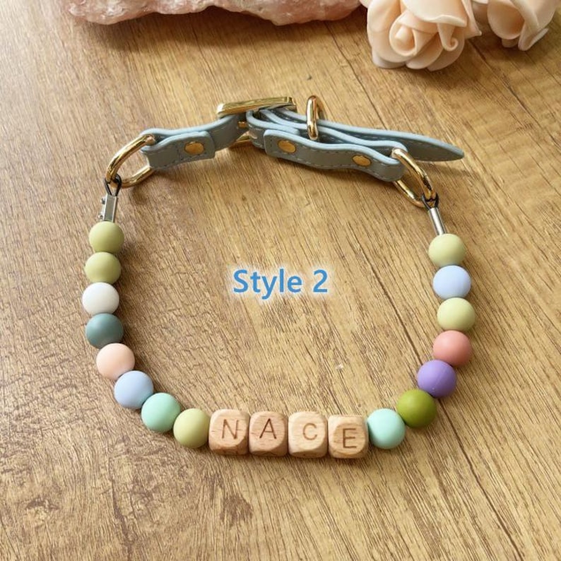 May include: A light blue dog collar with gold-colored hardware and a beaded section. The beads are pastel colors, and the wooden letter beads spell out "NACE". The text "Style 2" is also visible.