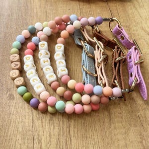 May include: A collection of colorful dog collars and beaded necklaces. The necklaces feature wooden letter beads spelling out "DANCE" and "NACE". The collars are leather in various pastel colors with gold-tone hardware.