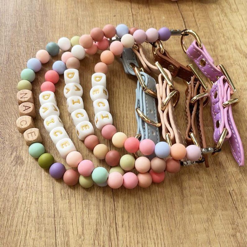 May include: A collection of colorful dog collars and beaded necklaces. The necklaces feature wooden letter beads spelling out "DANCE" and "NACE". The collars are leather in various pastel colors with gold-tone hardware.