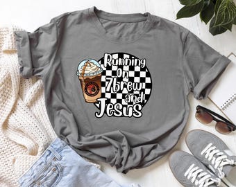 May include: Grey t-shirt featuring the text "Running on 7brew and Jesus" within a black and white chequered circle. A cartoon coffee drink with whipped cream is on the left.