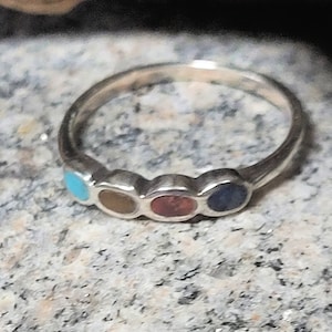 May include: A silver ring with five colorful stones set in a row. The stones are turquoise, brown, red, blue, and black.