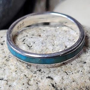May include: A silver ring with a thin band of turquoise inlay. The ring is marked "925" on the inside.