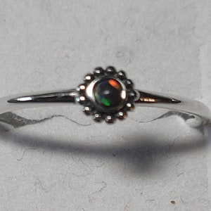 May include: A silver ring with a black opal gemstone set in a small, beaded flower design.