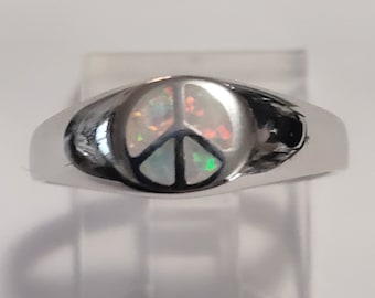 Puede incluir: Un anillo de plata con un diseño de signo de paz engastado con una ópalo iridiscente.
