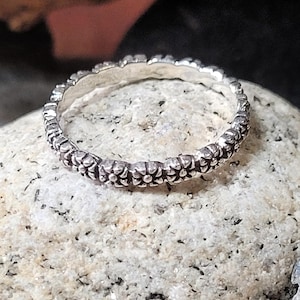 May include: A silver ring with a textured design of small flower shapes around the band.