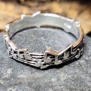 May include: A silver ring with a design of musical notes. The ring is made of sterling silver and has a polished finish.