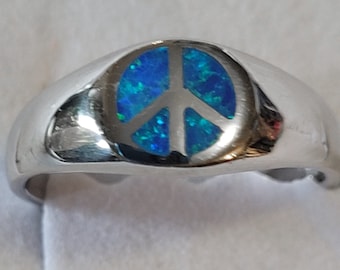 Puede incluir: Un anillo de plata con un símbolo de paz de ópalo azul.