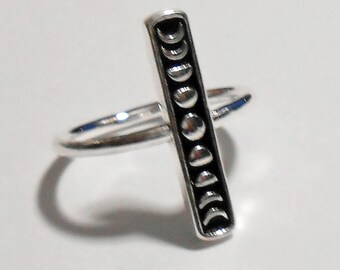 May include: A silver ring with a vertical bar featuring a design of eight crescent moons in different phases.