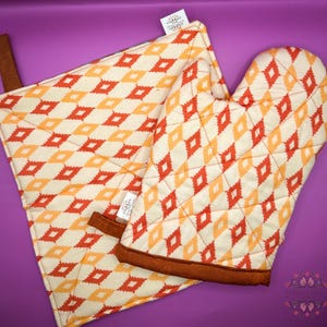 May include: A set of two kitchen pot holders with a diamond pattern in shades of orange, yellow, and white. The pot holders are made of cotton and have a brown trim.