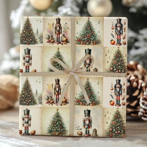 Op de afbeelding: Een rechthoekige geschenkdoos verpakt in crèmekleurig papier met een herhalend rasterpatroon van notenkrakers en versierde kerstbomen, vastgebonden met een dun, glinsterend goudkleurig lint dat in het midden tot een strik is gevormd.
