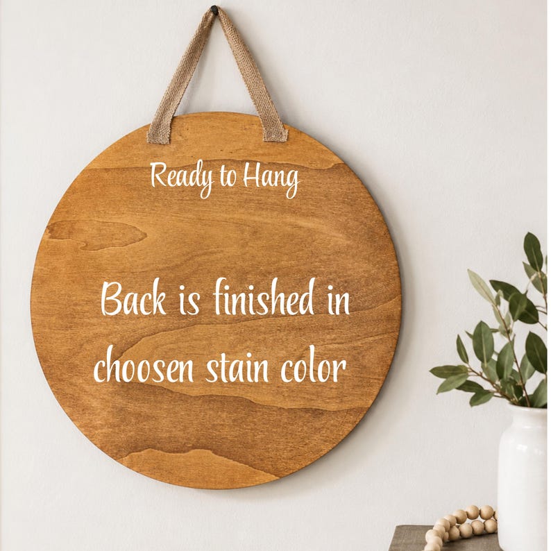 K&ouml;nnte beinhalten: Runder Holzschild mit hellbrauner Beize, fertig zum Aufh&auml;ngen. Das Schild hat eine nat&uuml;rliche Holzmaserung und eine beige Stoffschlaufe zum Aufh&auml;ngen. Der Text auf dem Schild lautet "Ready to Hang" und "Back is finished in chosen stain color."