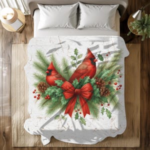 May include: A white blanket featuring a festive design with two red cardinal birds, a red bow, pinecones, holly, and berries. The blanket has a distressed, textured background, creating a rustic, holiday theme.