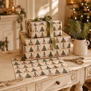Pode incluir: Duas caixas de presente retangulares embrulhadas em papel creme com um padr&atilde;o de grade repetido de &aacute;rvores de Natal verdes e quebra-nozes. A caixa superior est&aacute; amarrada com uma fita de veludo verde-oliva. Papel a condizer e tesoura dourada.
